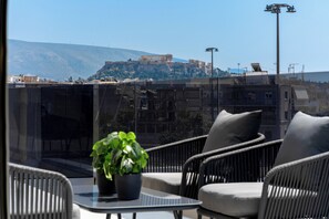A balcony with wicker furniture and a potted plant, overlooking a historic building on a hill. - Acropolis View - Stylish City Penthouse (Athens)