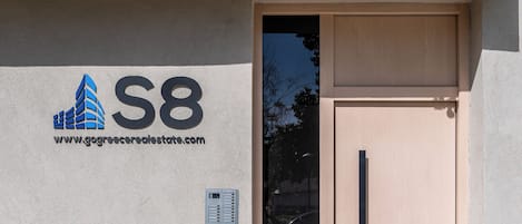 L'ingresso di un edificio con una porta color beige, una serratura con tastierino numerico e un indirizzo web sulla parete.