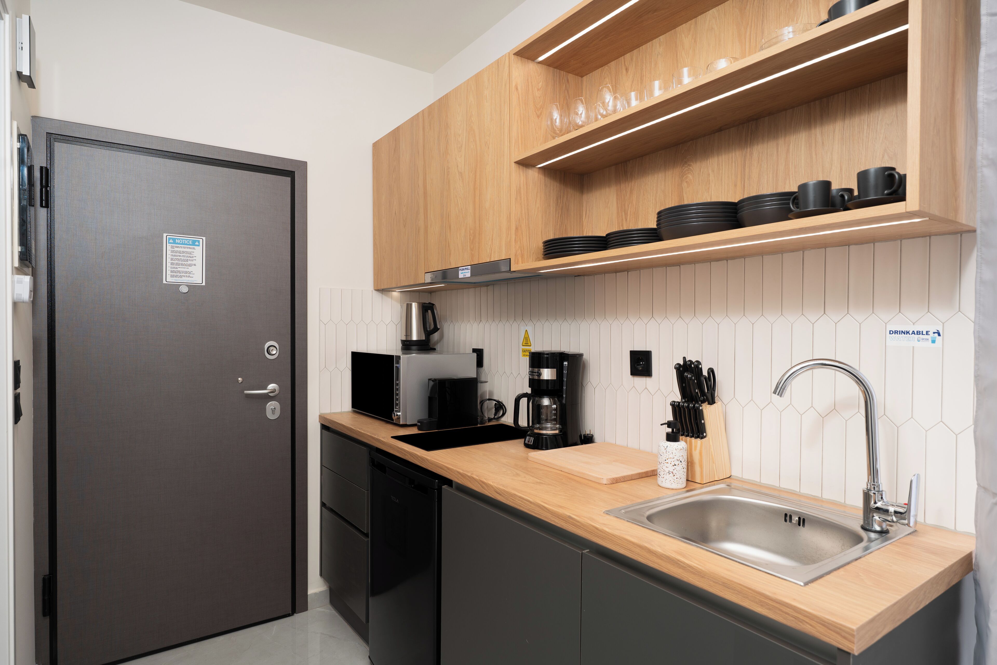 Une cuisine moderne dotée d’un évier en acier inoxydable, d’un plan de travail en bois et d’appareils électroménagers noirs.