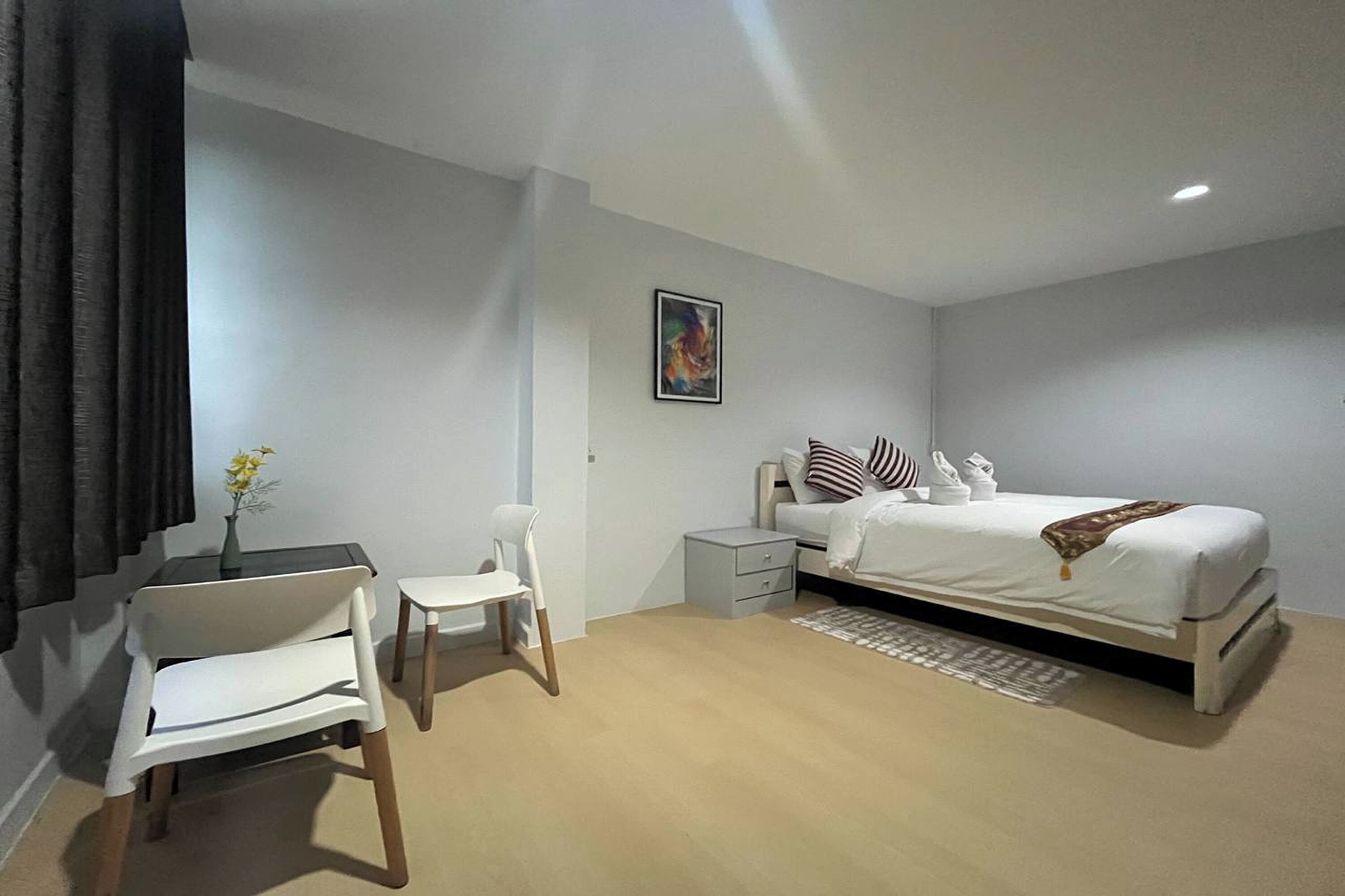 Un dormitorio moderno con cama, mesitas de noche, una silla y una pequeña mesa con un florero.