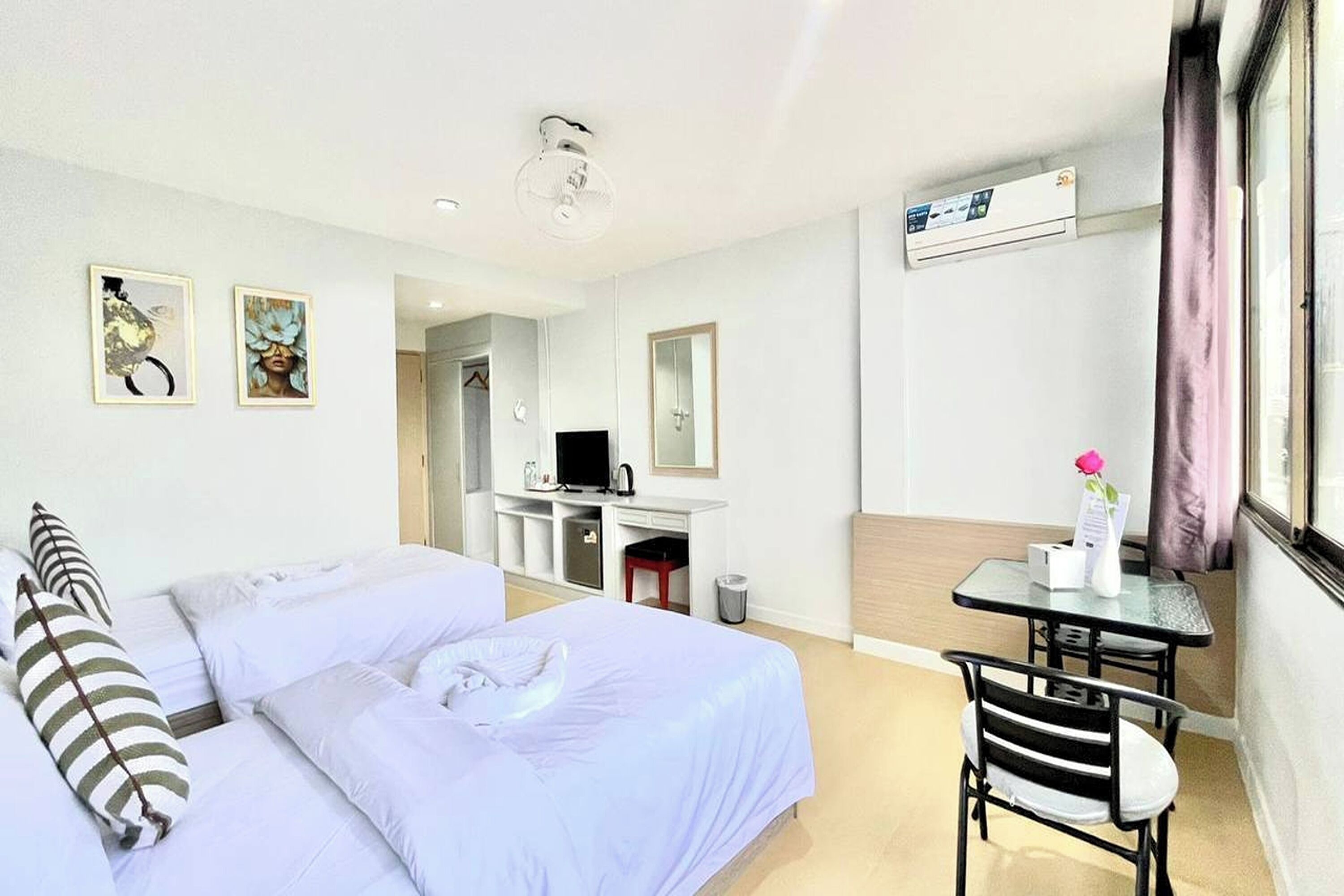 A hotel room with a bed, a desk, a chair, and a small table with a vase of flowers.