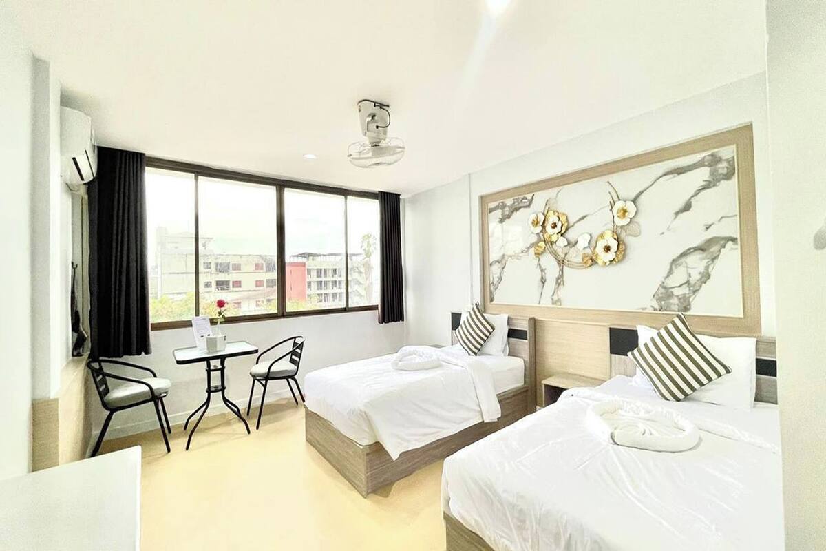 Una habitación de hotel con dos camas, una mesita pequeña, sillas y un ventanal grande.