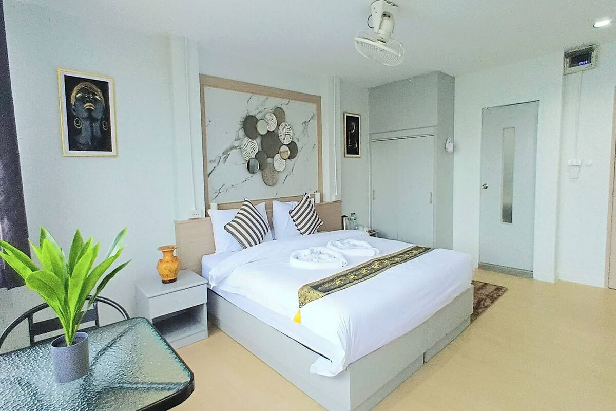 Una habitación de hotel moderna con una cama grande, una mesita de noche con lámpara, una planta en maceta y un adorno de pared de mármol.