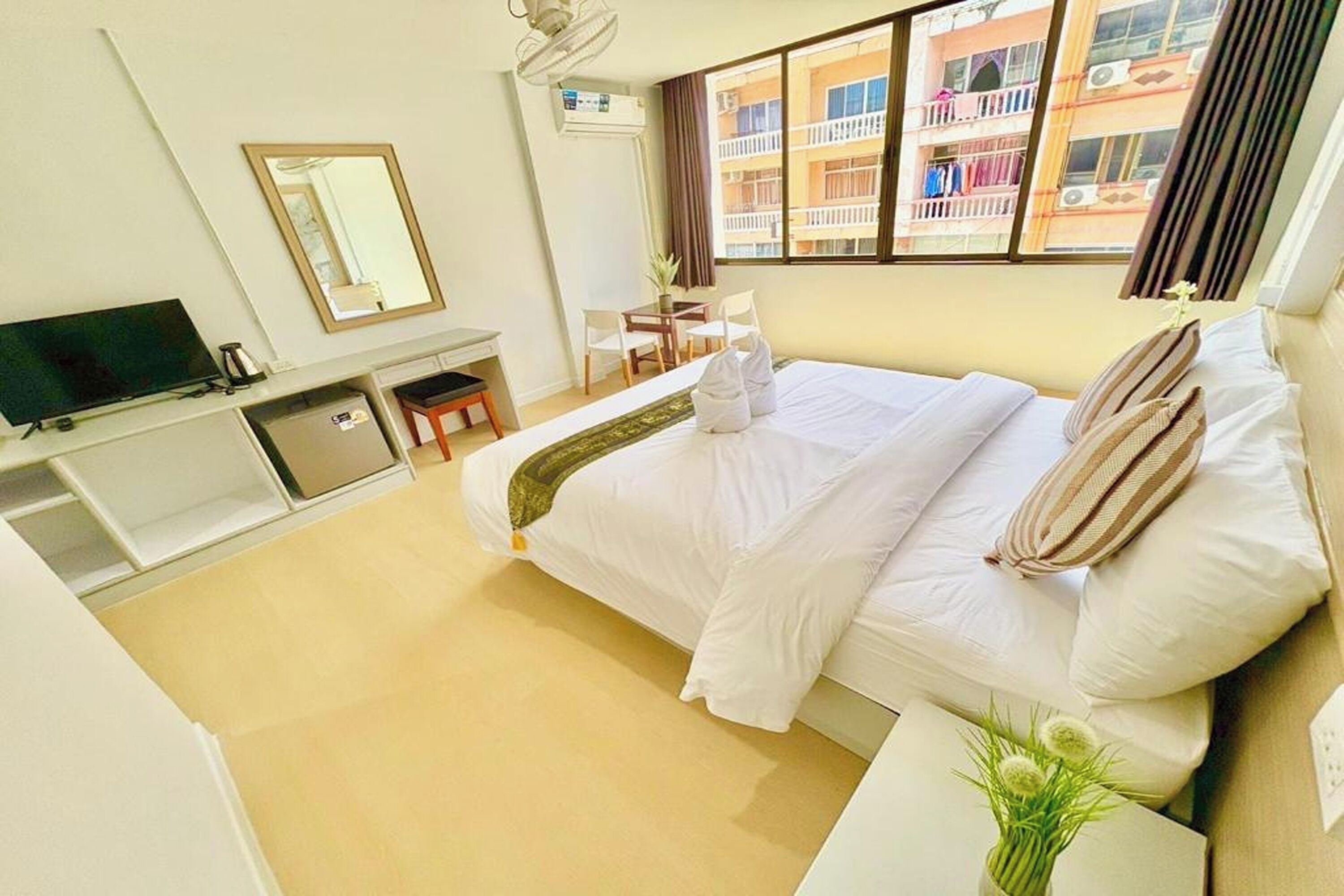 A hotel room with a bed, a TV, a desk, and a window with a view of buildings.