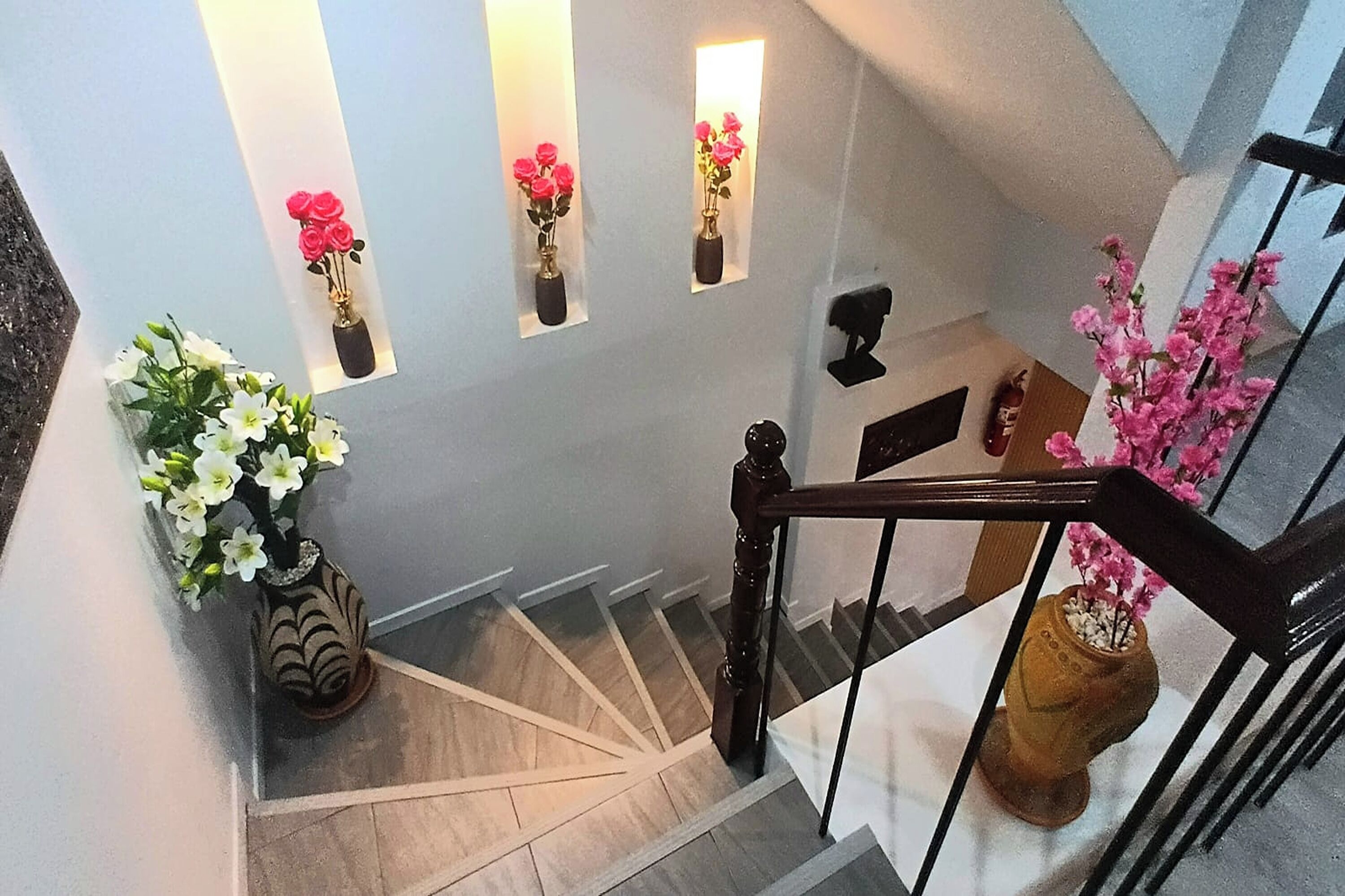 A staircase with a wooden handrail, a vase with white flowers, and a vase with pink flowers on the wall.