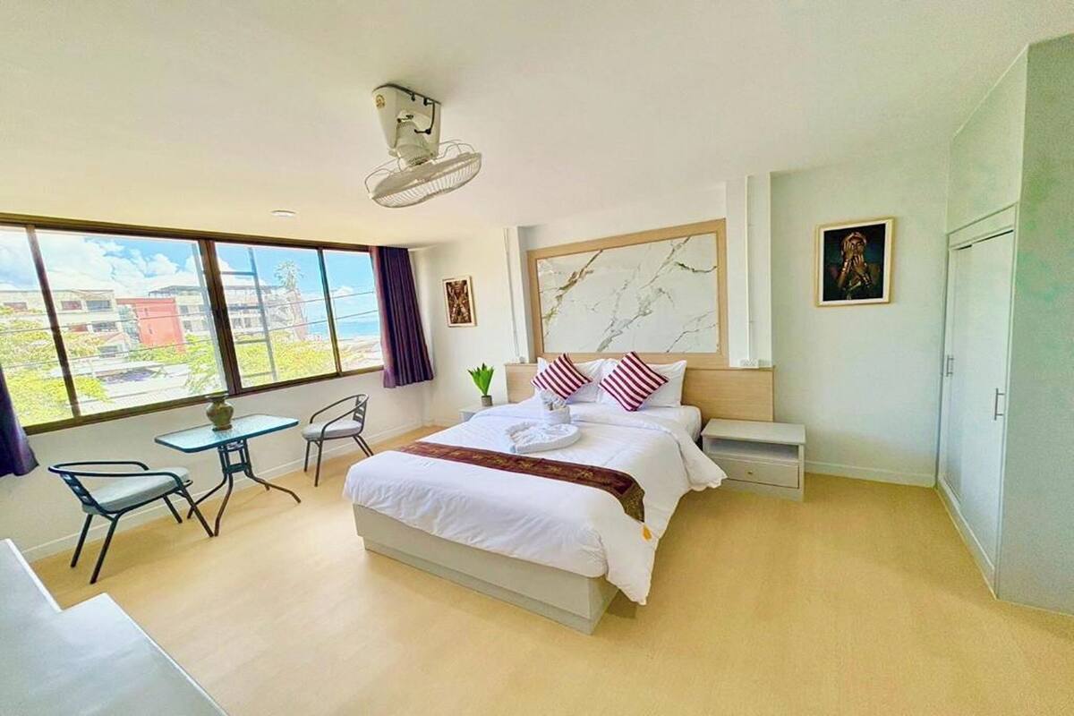 Una habitación de hotel moderna con una cama grande, un escritorio y una silla. Se ve una ventana con vistas a edificios.