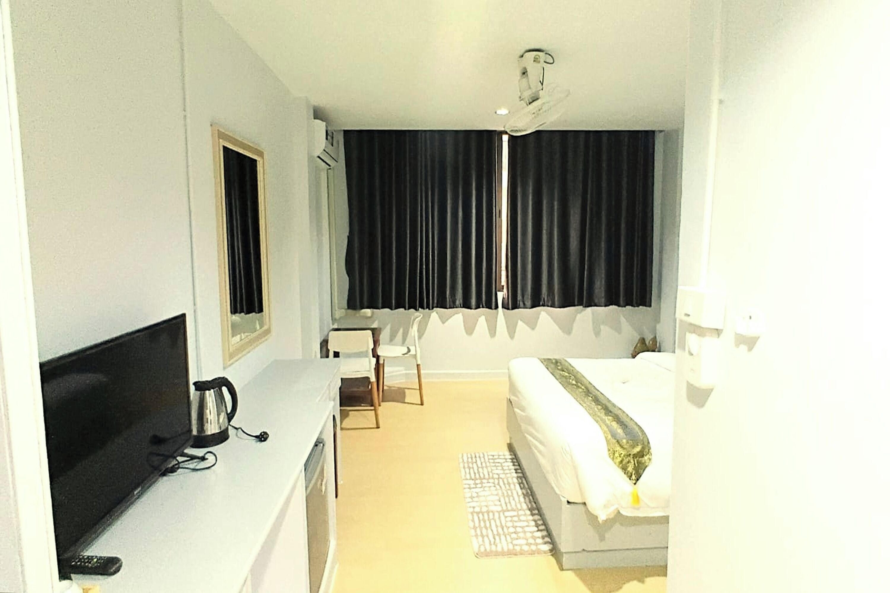Habitación de hotel con una cama, un escritorio con televisor, una silla y una ventana con cortinas.