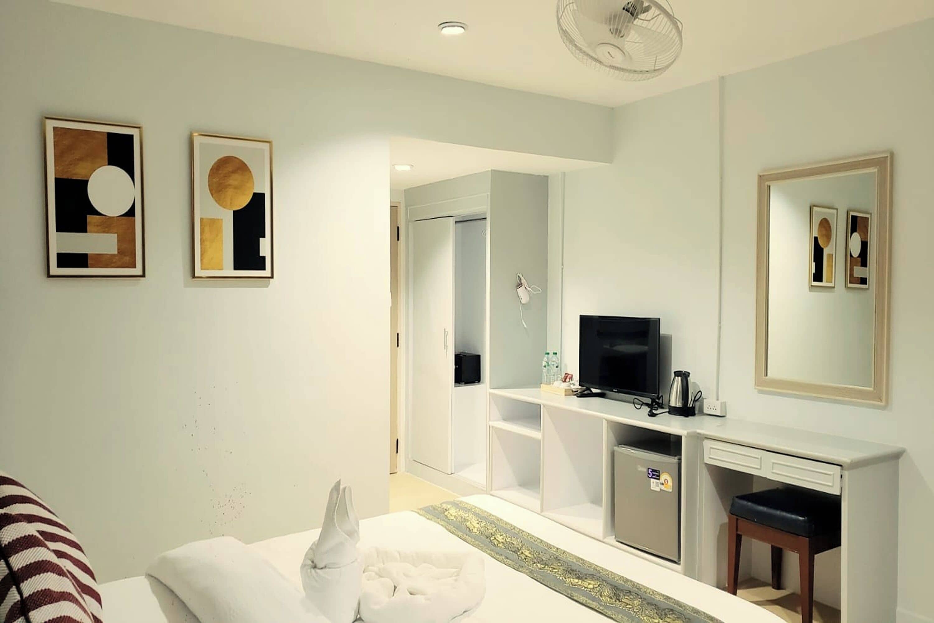 A hotel room with a bed, a desk with a TV, a minibar, and a mirror.