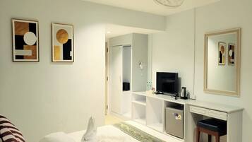 A hotel room with a bed, a desk with a TV, a minibar, and a mirror.