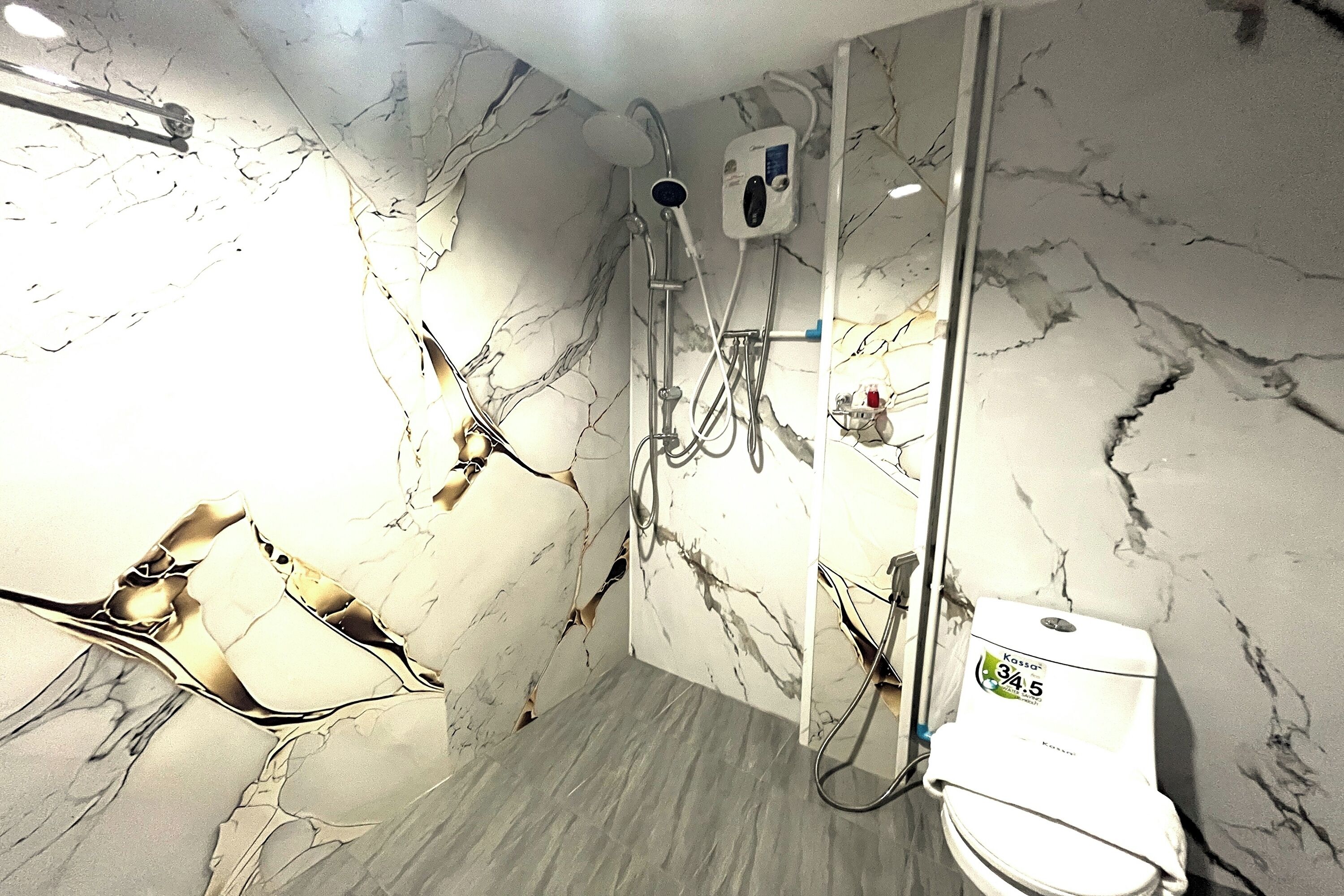 A bathroom with a marble wall, a shower, and a toilet.