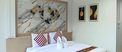 A hotel room with a marble-patterned wall art, a neatly made bed with white linens and a red-striped pillow, and two framed artworks on the wall.