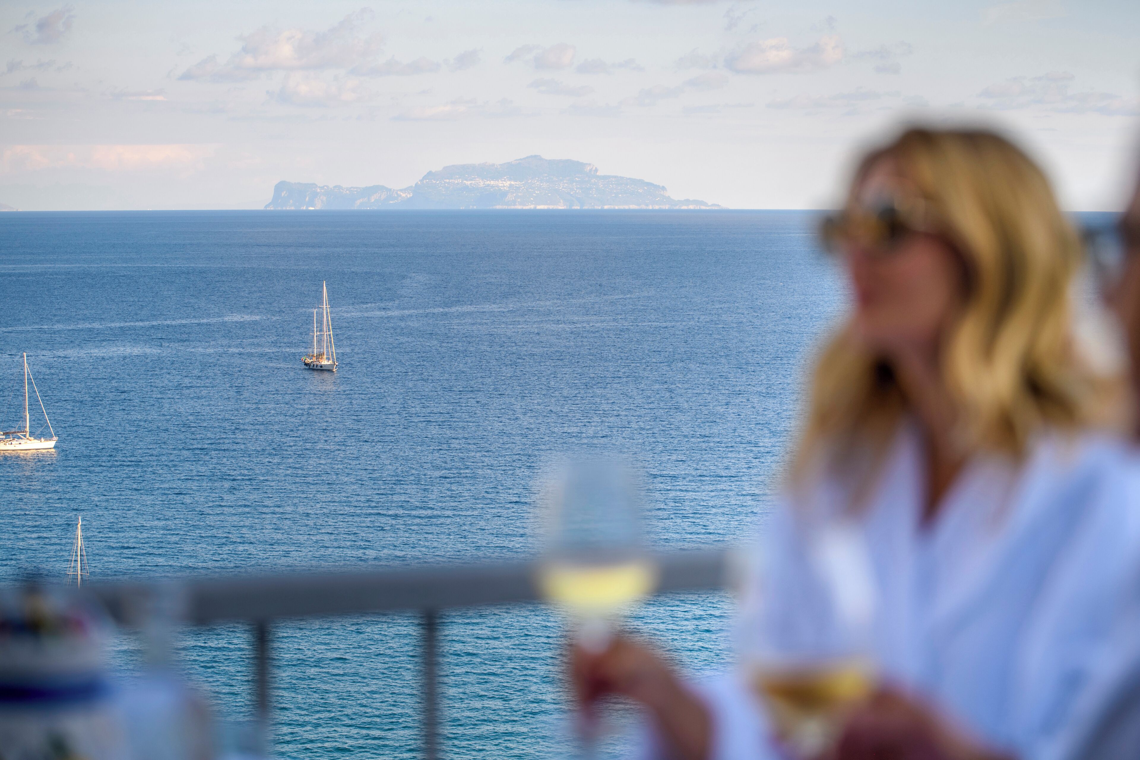 A coastal scene with a sailboat on the water and a distant landmass.