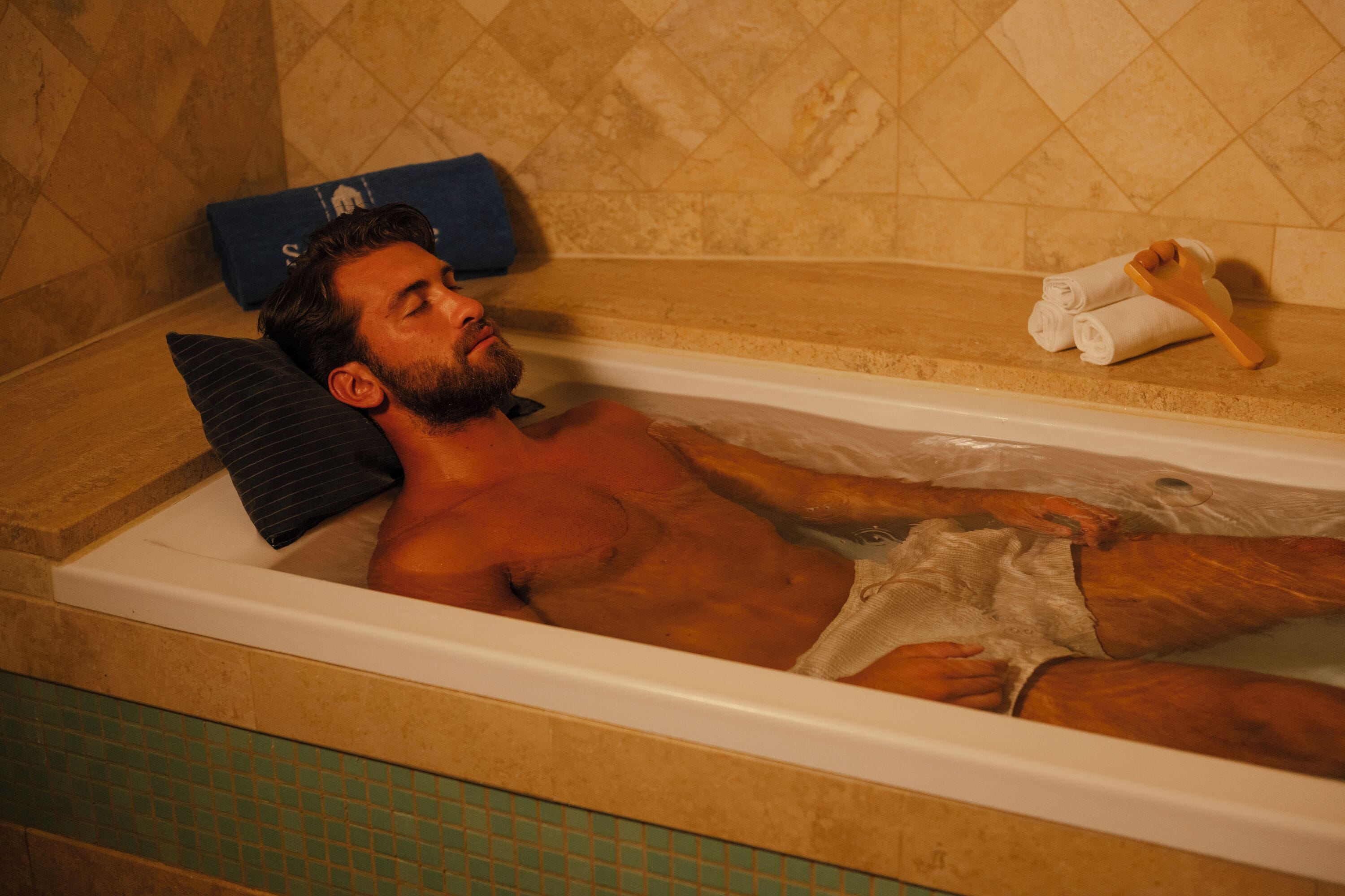 Un hombre recostado en una bañera con una toalla y un cepillo.