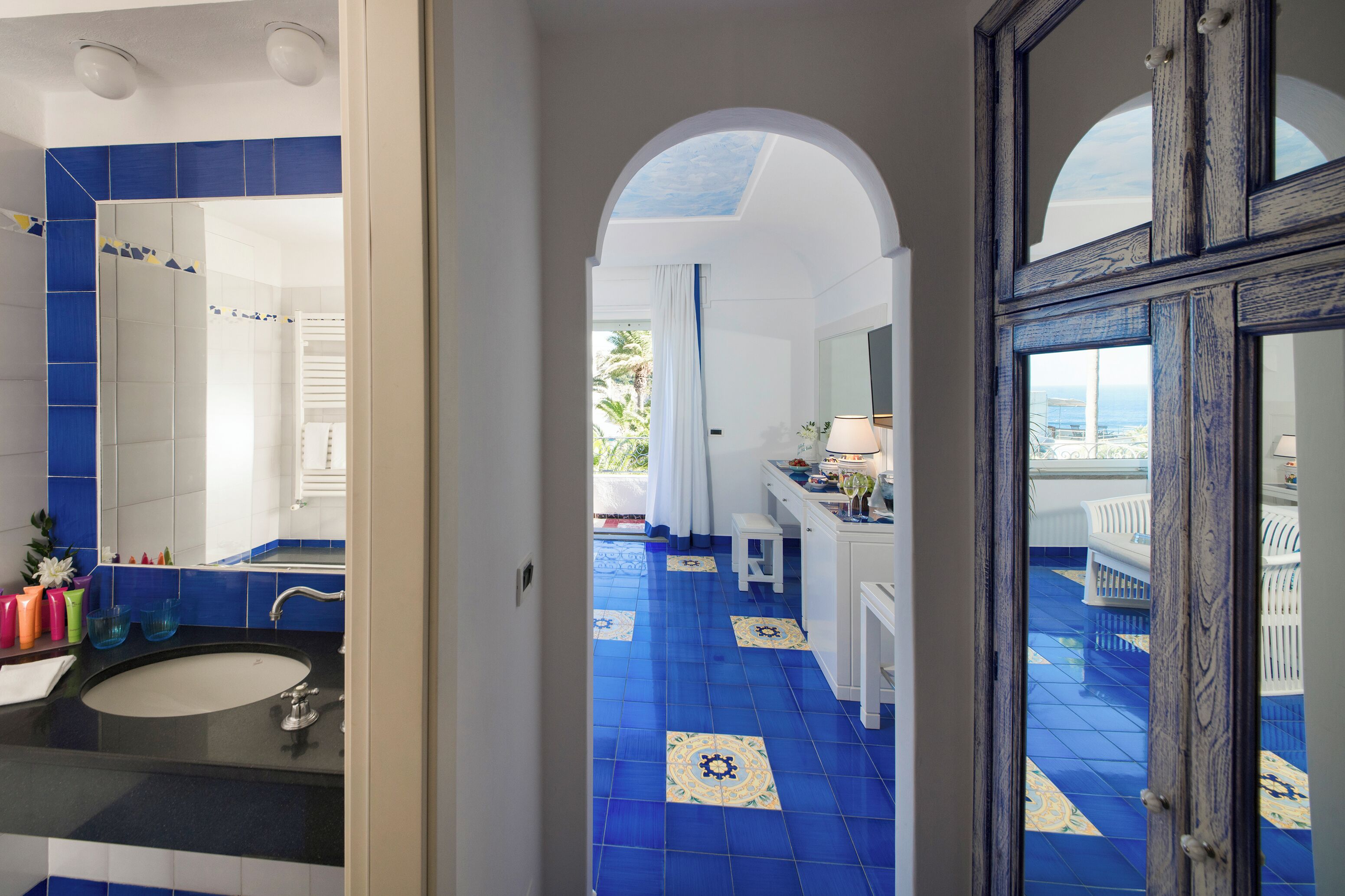 A bathroom with a large mirror, a sink, and blue-tiled flooring.