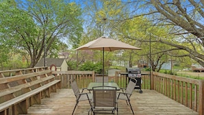 Une terrasse en bois avec une table et des chaises, un barbecue et une pergola avec un parasol.