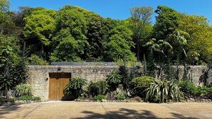 A stone building with a wooden door, surrounded by lush greenery and trees.