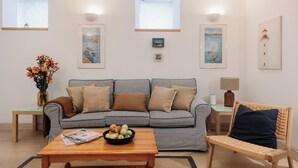 A living room with a striped sofa, a wooden coffee table with fruit, a wicker chair, and artwork on the walls.