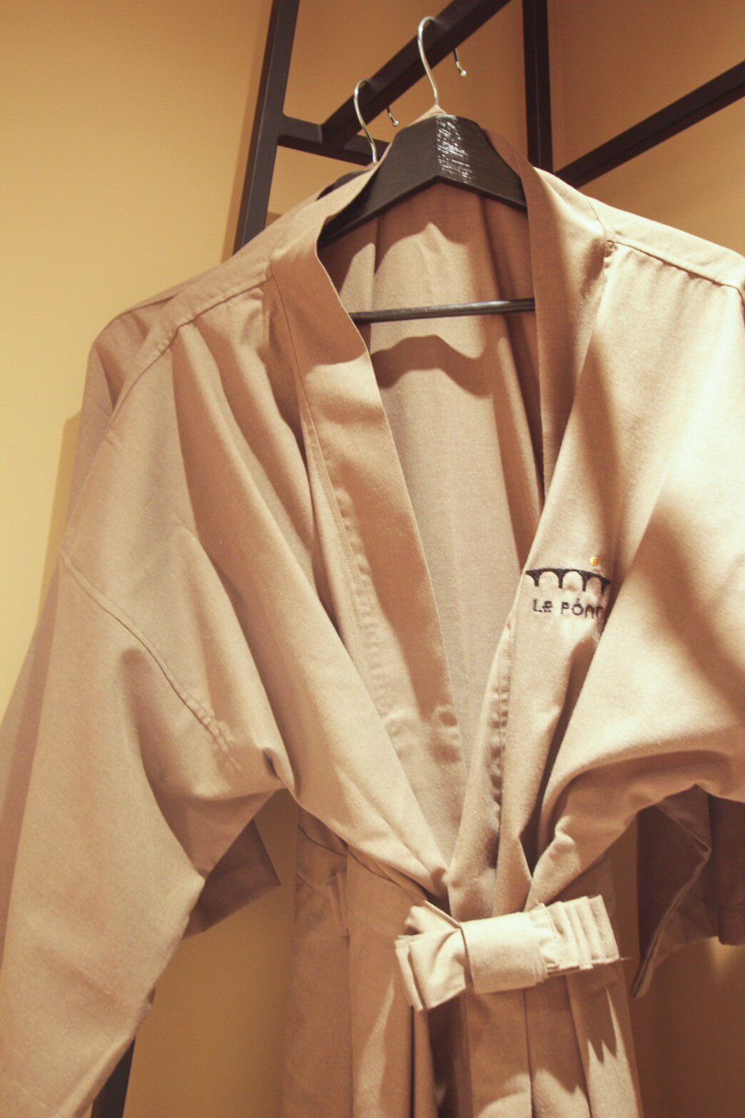 A beige shirt with a V-neck and a tie at the waist, hanging on a black hanger.