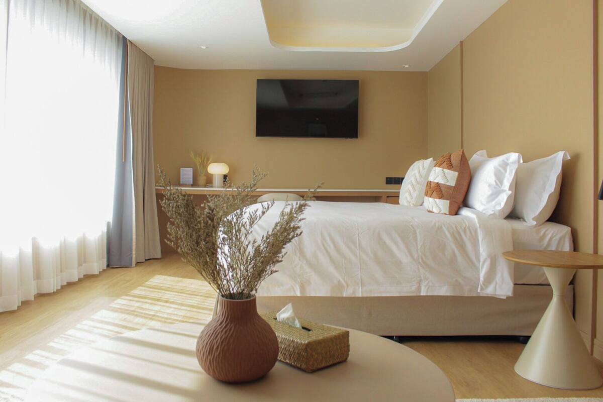 Ein modernes Hotelzimmer mit Bett, Nachttisch, Lampe und einer Vase mit Trockenpflanzen.