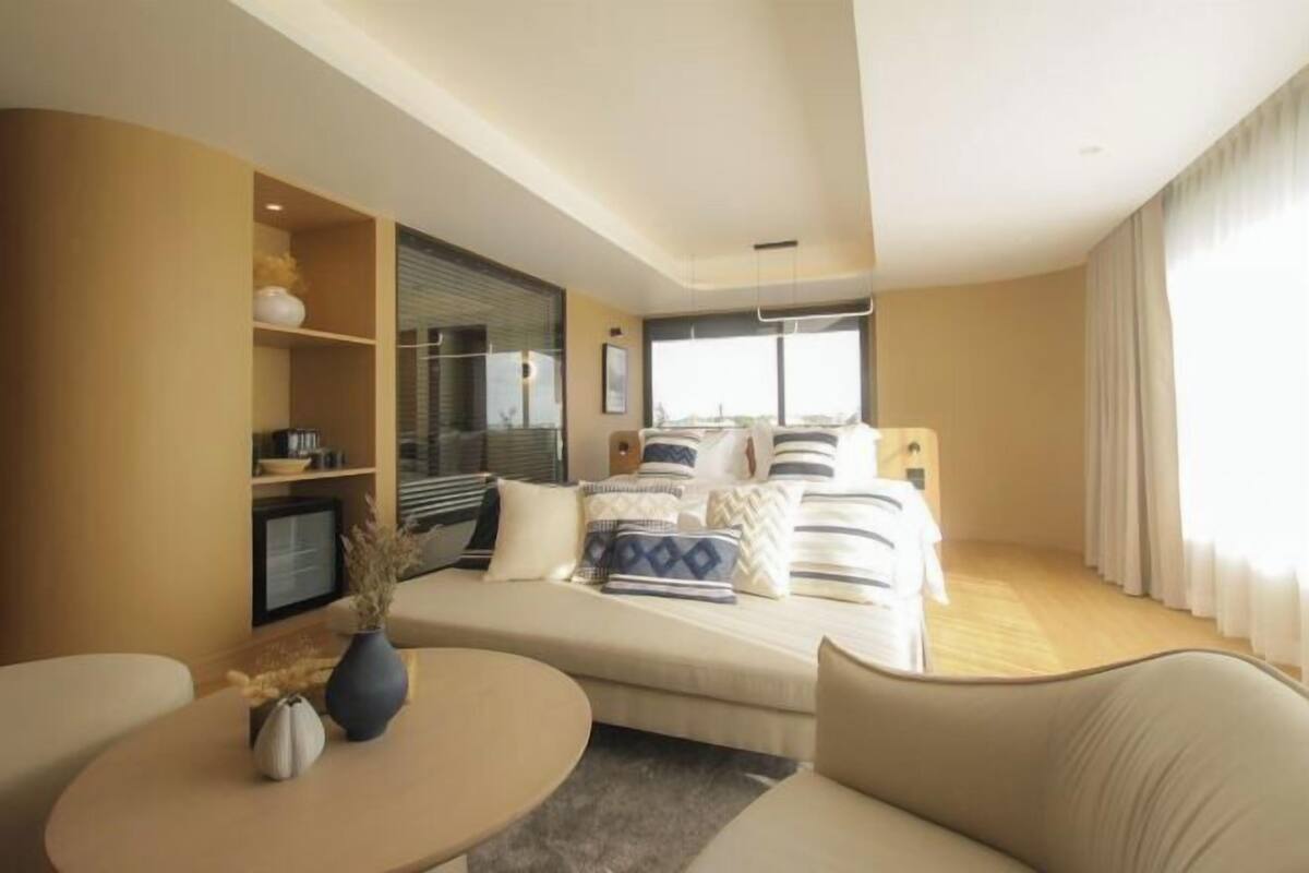 A modern hotel room with a bed, a sofa, a small table, and a TV.