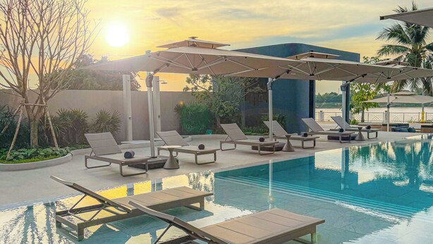 Una piscina con sillas de descanso y sombrillas, rodeada por un jardín ajardinado.