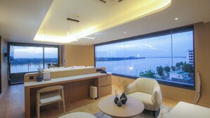 Habitación de hotel moderna con un ventanal grande que ofrece vistas al agua y al paisaje urbano.