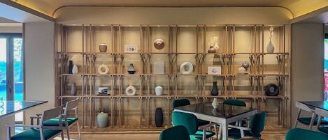 Un interior moderno con una mesa de vidrio central rodeada por sillas color turquesa, una estantería de madera con varios objetos decorativos y una unidad de aire acondicionado instalada en el techo.