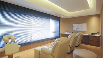 A modern spa room with massage chairs, a reception desk, and a large window with blinds.