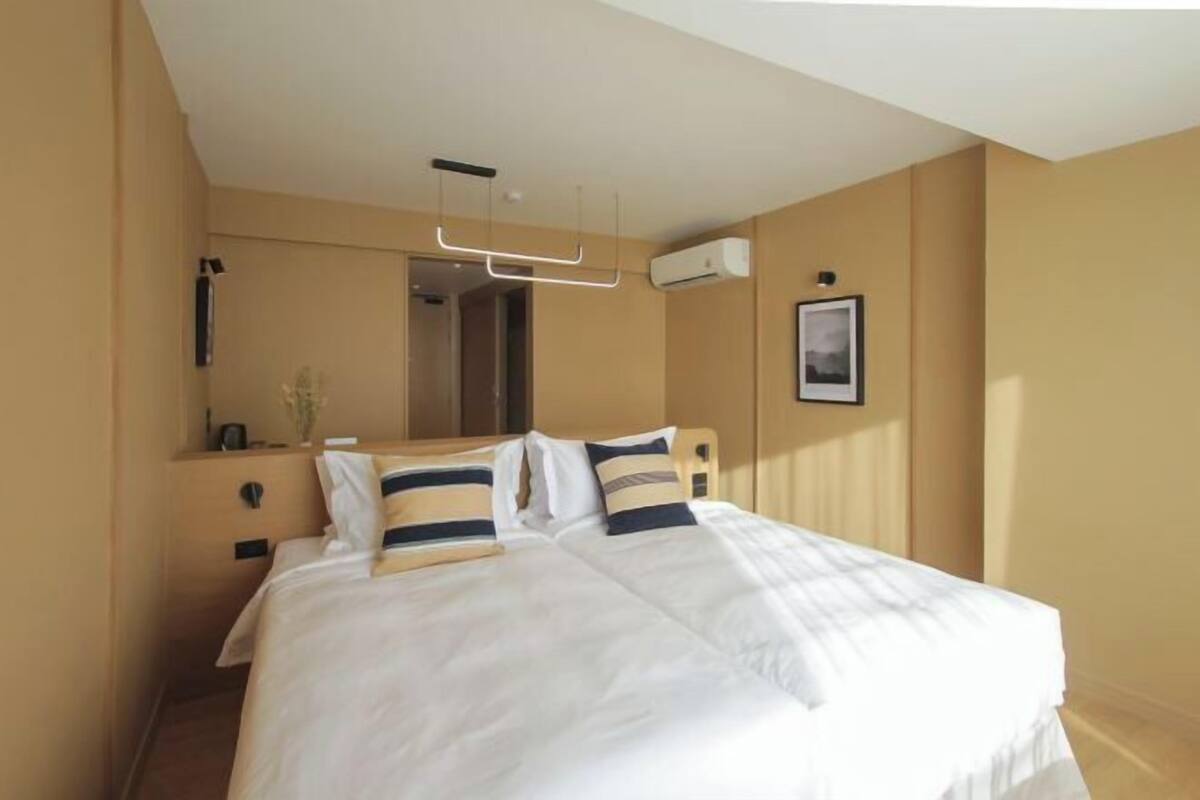 A hotel room with a large bed, a bedside table, a mirror, and a wall-mounted air conditioning unit.