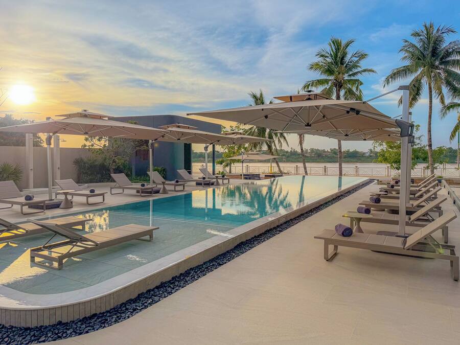 Zona de piscina con tumbonas, sombrillas y una vista despejada del atardecer.