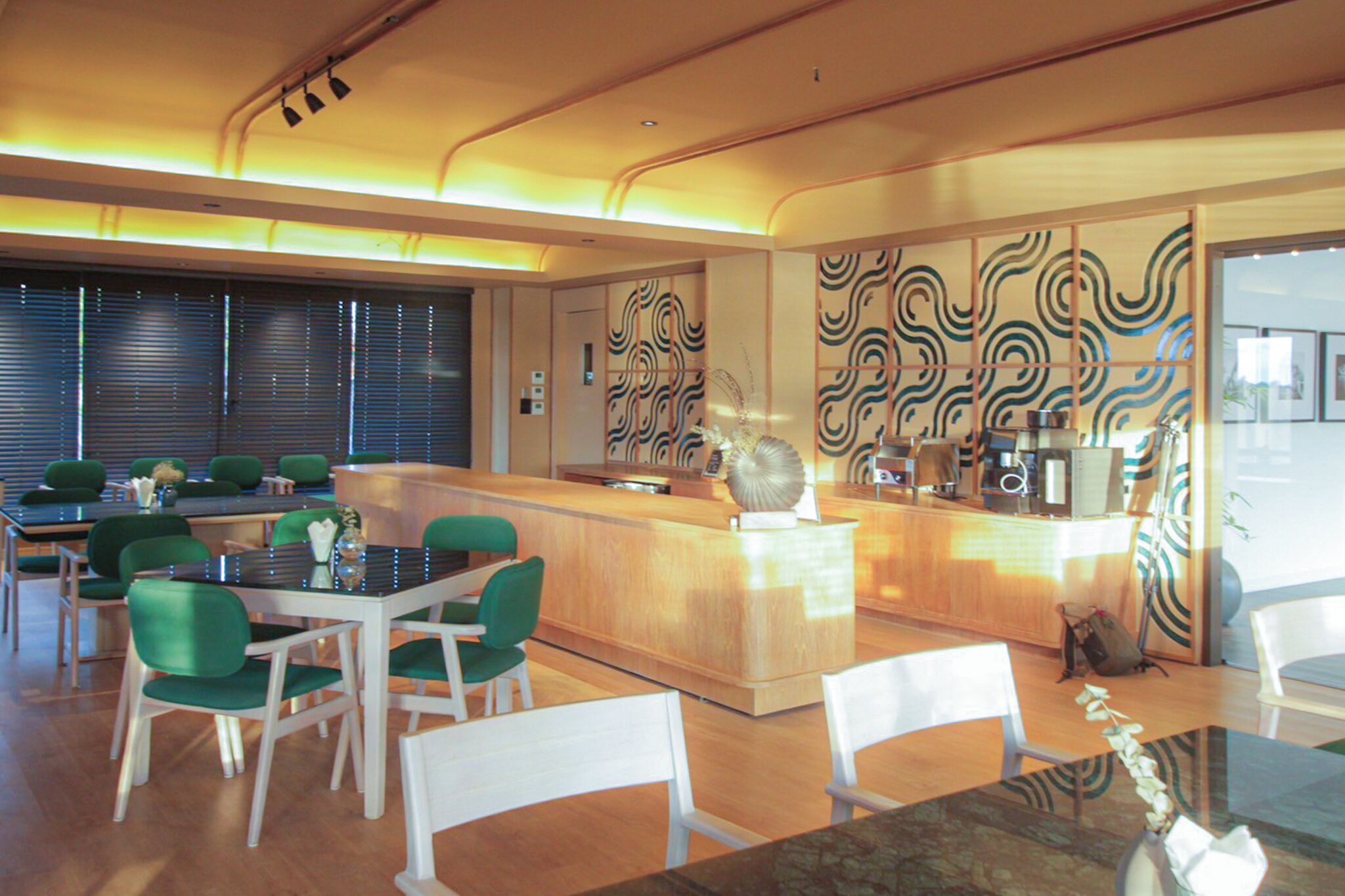 A modern hotel lobby with a reception desk, green chairs, and a wooden floor.