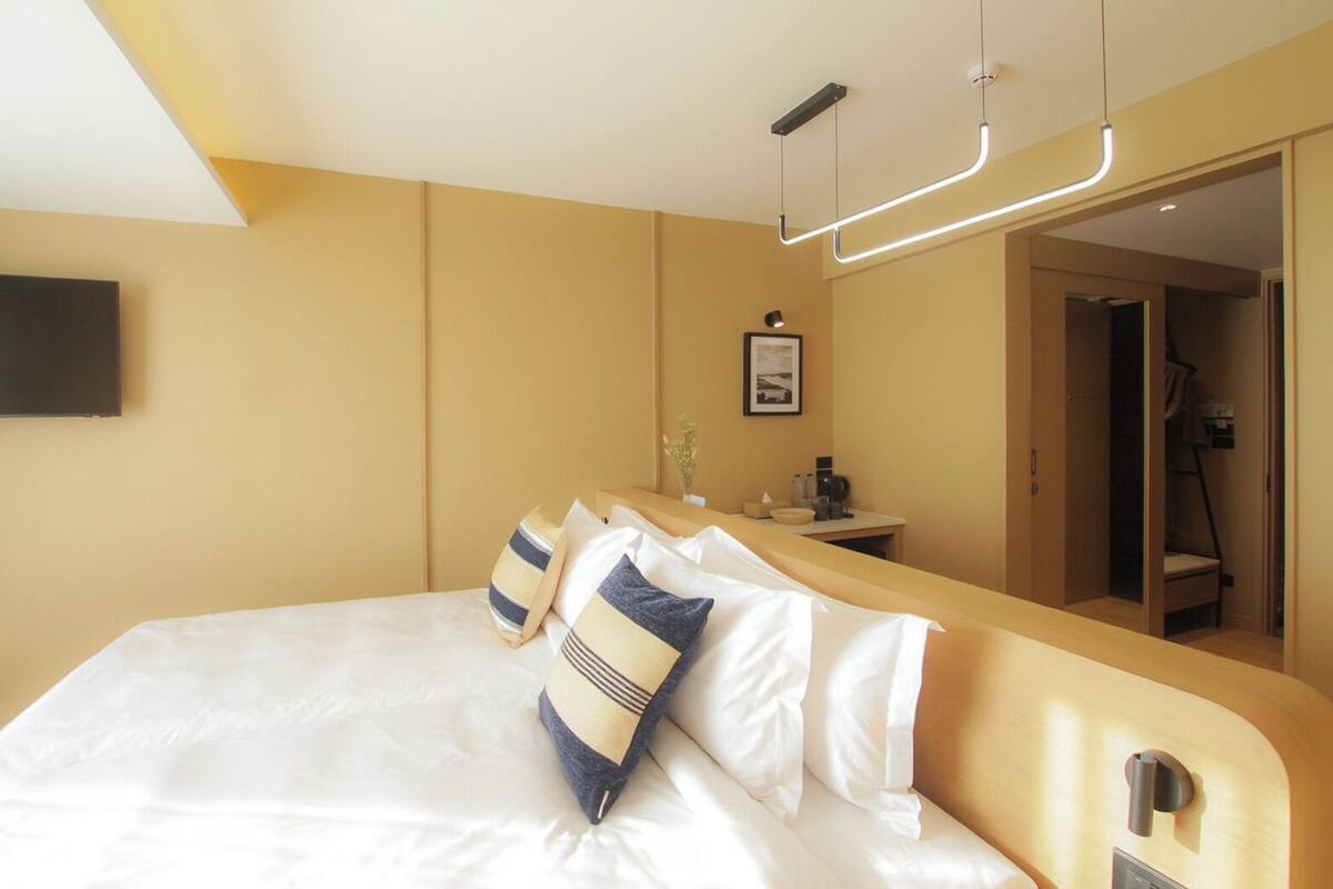 Ein Hotelzimmer mit einem großen Bett, einem Nachttisch, einem Spiegel und einem an der Wand befestigten Fernseher.