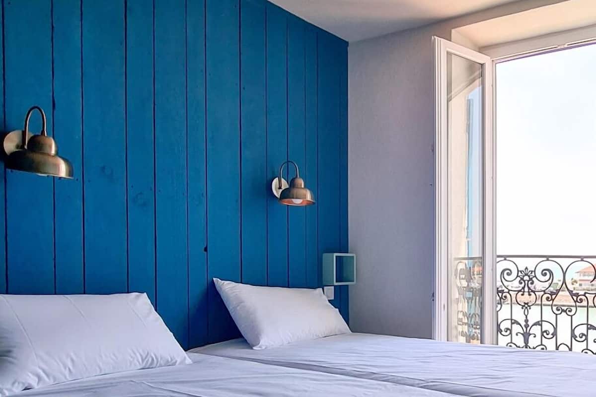 A hotel room with two beds, a blue accent wall, and a balcony with wrought iron railings.