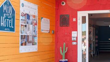 A hotel entrance with a wooden facade, a cactus in a blue pot, and a sign reading "Mon petit HOTEL".
