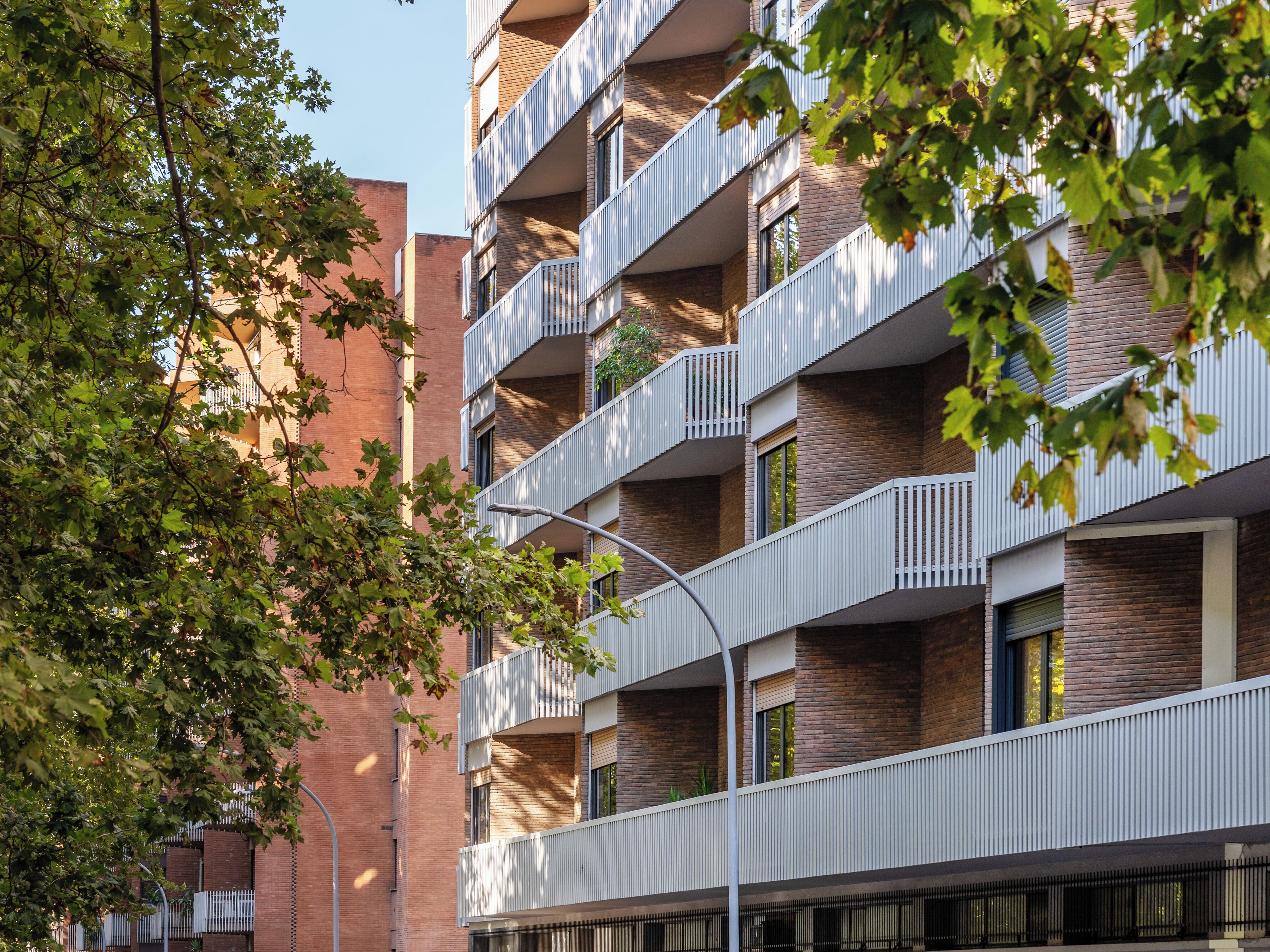 Ein mehrgeschossiges Wohnhaus mit Balkonen, Ziegel Fassade und umliegenden Bäumen.