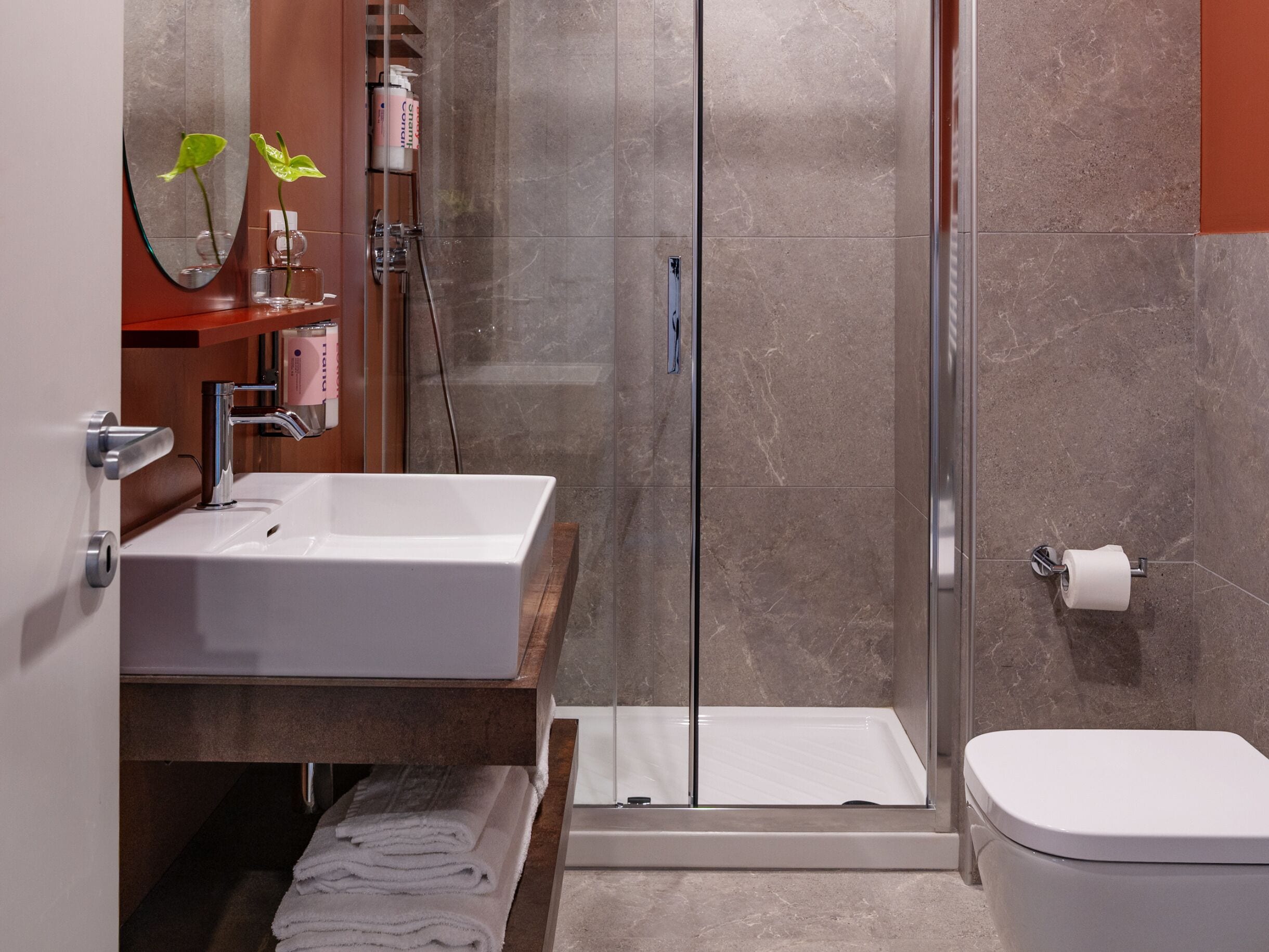 A modern bathroom with a white sink, a glass shower enclosure, and a toilet.