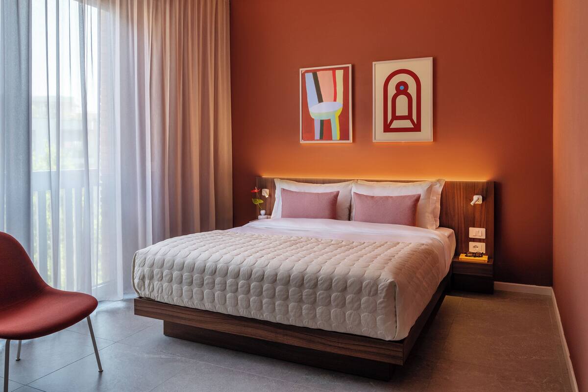 Ett hotellrum med en stor säng, en röd stol och två konstverk som hänger på väggen.