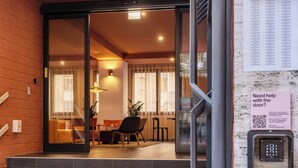 A hotel entrance with a glass door, a staircase, and a sign offering help with the door. - Numa Rome Trastevere (Rome)
