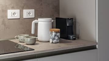 A kitchen counter with a coffee maker, a kettle, a jar with tea bags, and a black appliance.