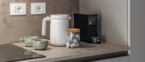 A kitchen counter with a coffee maker, a kettle, a jar with tea bags, and a black appliance.