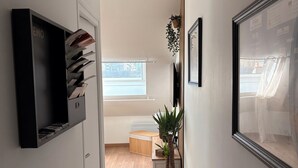 A hallway with a wooden floor, a black TV stand, a plant, and a framed picture on the wall. - Cathedral view apartment (Bayeux)