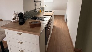 A compact kitchen with white cabinetry, a wooden countertop, and a built-in oven. - Cathedral view apartment (Bayeux)
