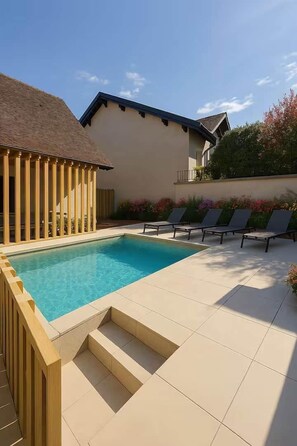 A swimming pool with a wooden deck and lounge chairs, surrounded by a house with a tiled patio. - House in village center and swimming pool (Chanaz)