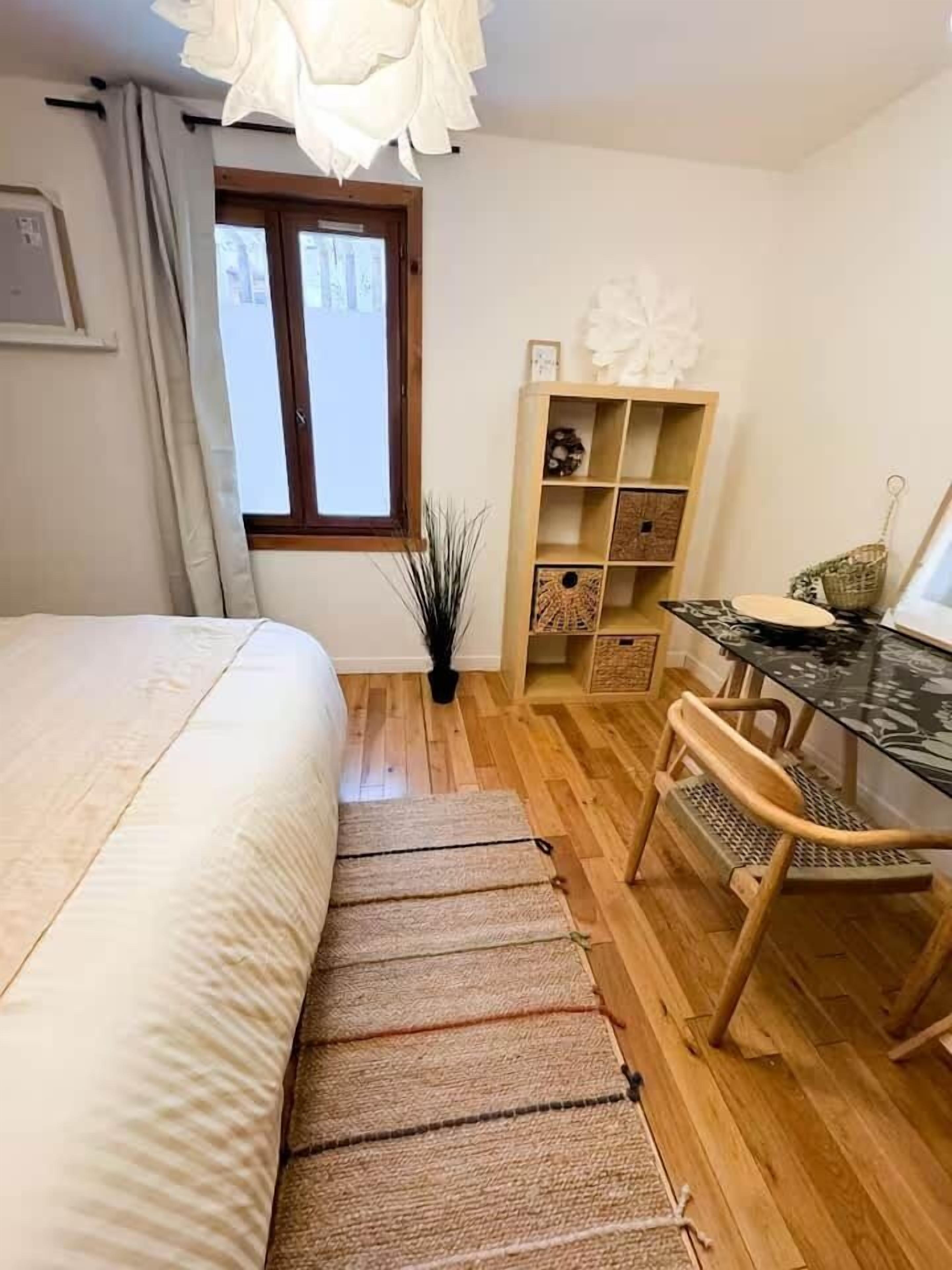 A bedroom with a bed, a desk, a chair, a small plant, and a window.