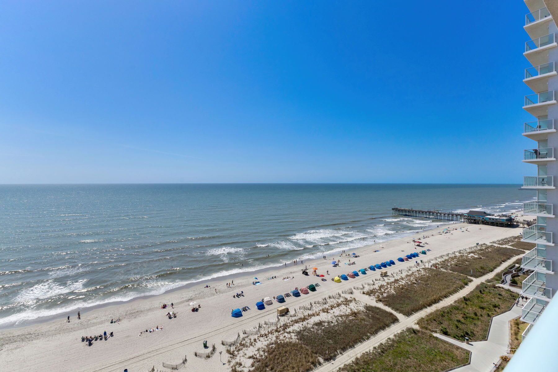 Uitzicht op een strand met een steiger, zandstrand en een hoog gebouw met balkons.