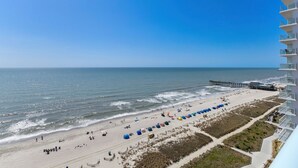 A beach view with a pier, sandy beach, and a high-rise building with balconies.