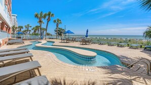 A pool area with lounge chairs, a winding pool, and a view of the ocean.