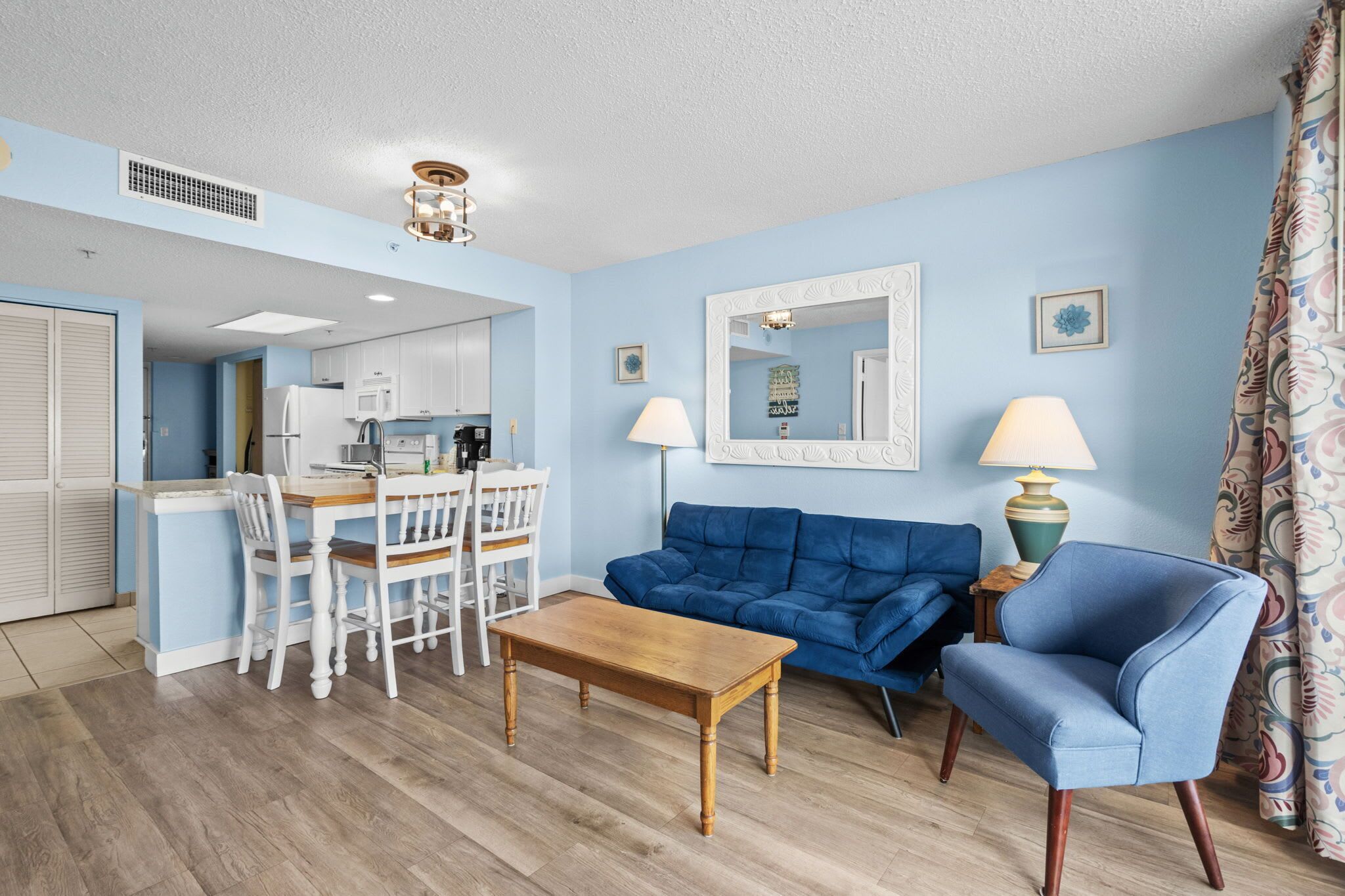 Un salon avec un canapé bleu, une table basse en bois et un coin repas comprenant des chaises blanches et une petite table.