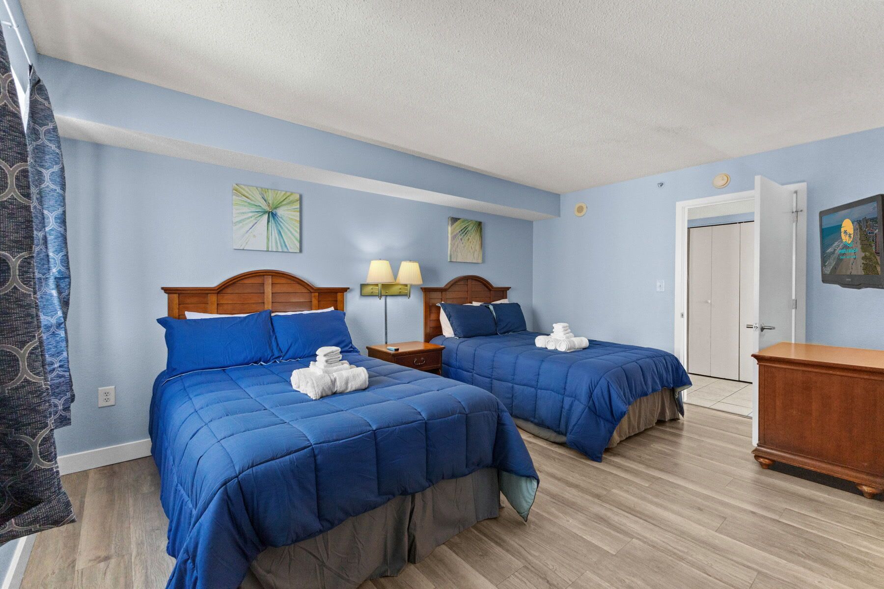 Quarto de hotel com duas camas, piso de madeira e porta para um banheiro.