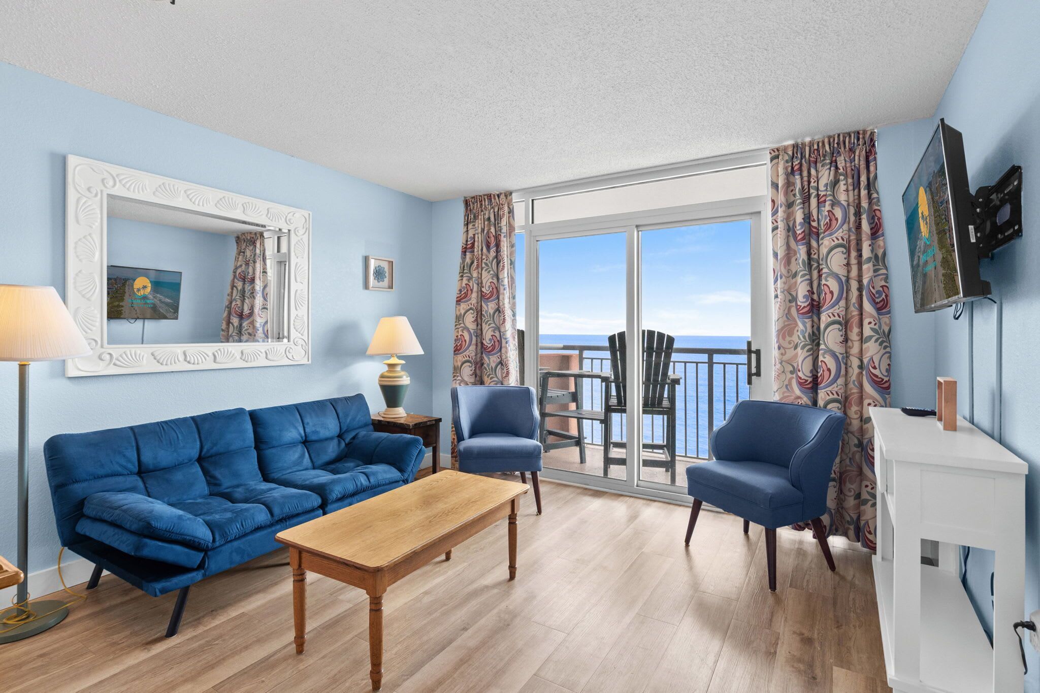 Ein Wohnzimmer mit einem blauen Sofa, zwei Sesseln, einem Holztisch und einem Balkon mit Blick.